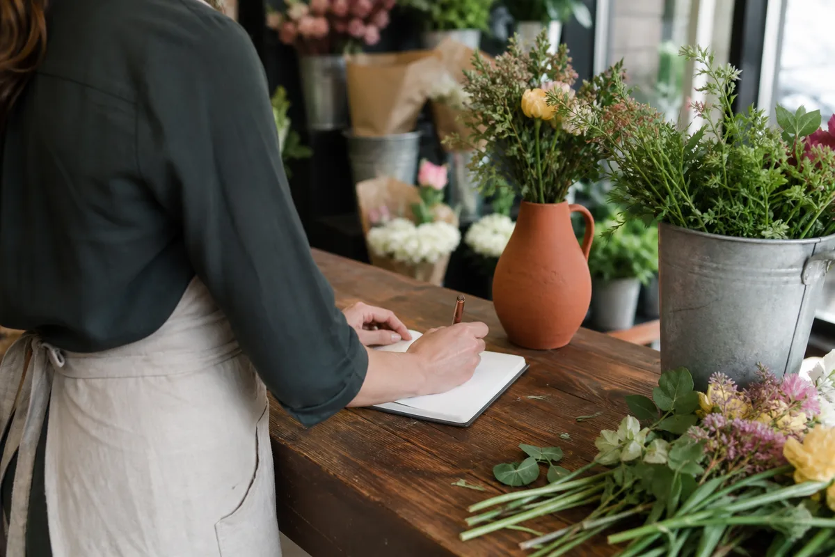 Fleuriste indépendante notant les chiffres de son trimestre dans un carnet au comptoir de sa boutique