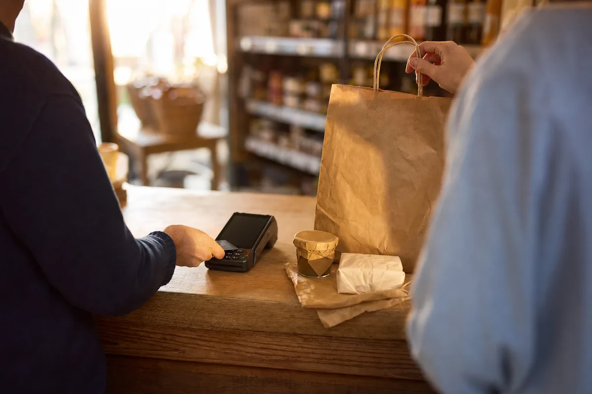 Détaillant encaissant un client dans un commerce de proximité en fin de journée